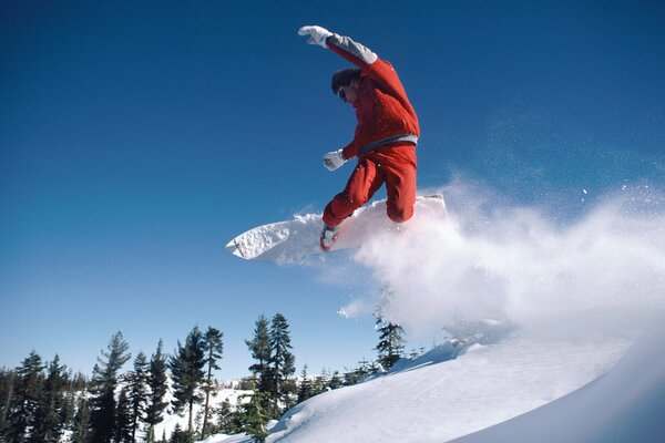 A snowboarder flies from a mountain against the background of a forest