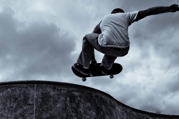 A skateboarder performs a trick against the background of gray clouds