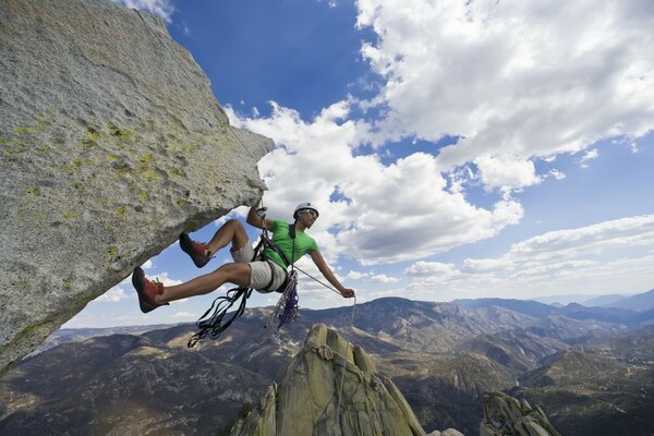 A climber on a rock against the background of mountains and a blue sky with clouds