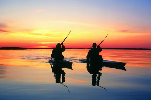 Dos personas en kayak nadan en la superficie del agua al atardecer del día