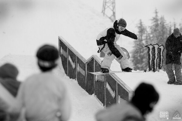 Snowboarder rotola su una tavola su una recinzione stretta di fronte agli spettatori