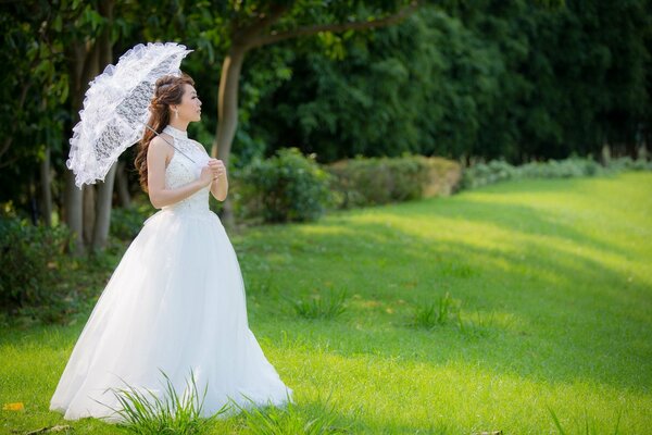 Chica asiática en un vestido de novia bajo un paraguas de verano