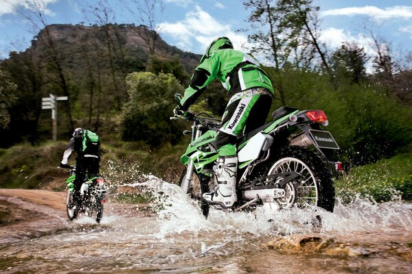 Dos motociclistas en negro y verde se trasladan al arroyo de la montaña