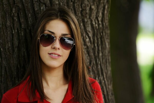 Brown-haired girl under a tree with dark glasses