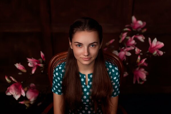 A girl in a polka dot dress is sitting in a chair against a background of flowers