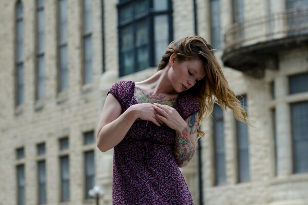 A girl with tattoos on her arm poses on the street