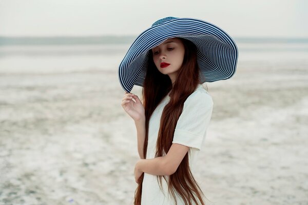 A girl in a white dress holds a striped wide-brimmed hat