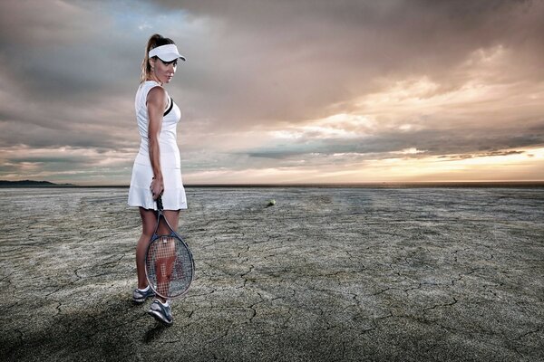 A tennis player in a white dress with a racket on the background of a desert landscape