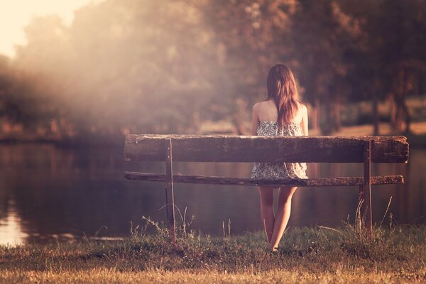 The girl is sitting on a bench on the bank of the river