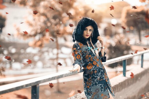 A girl stands in a coat under a leaf fall