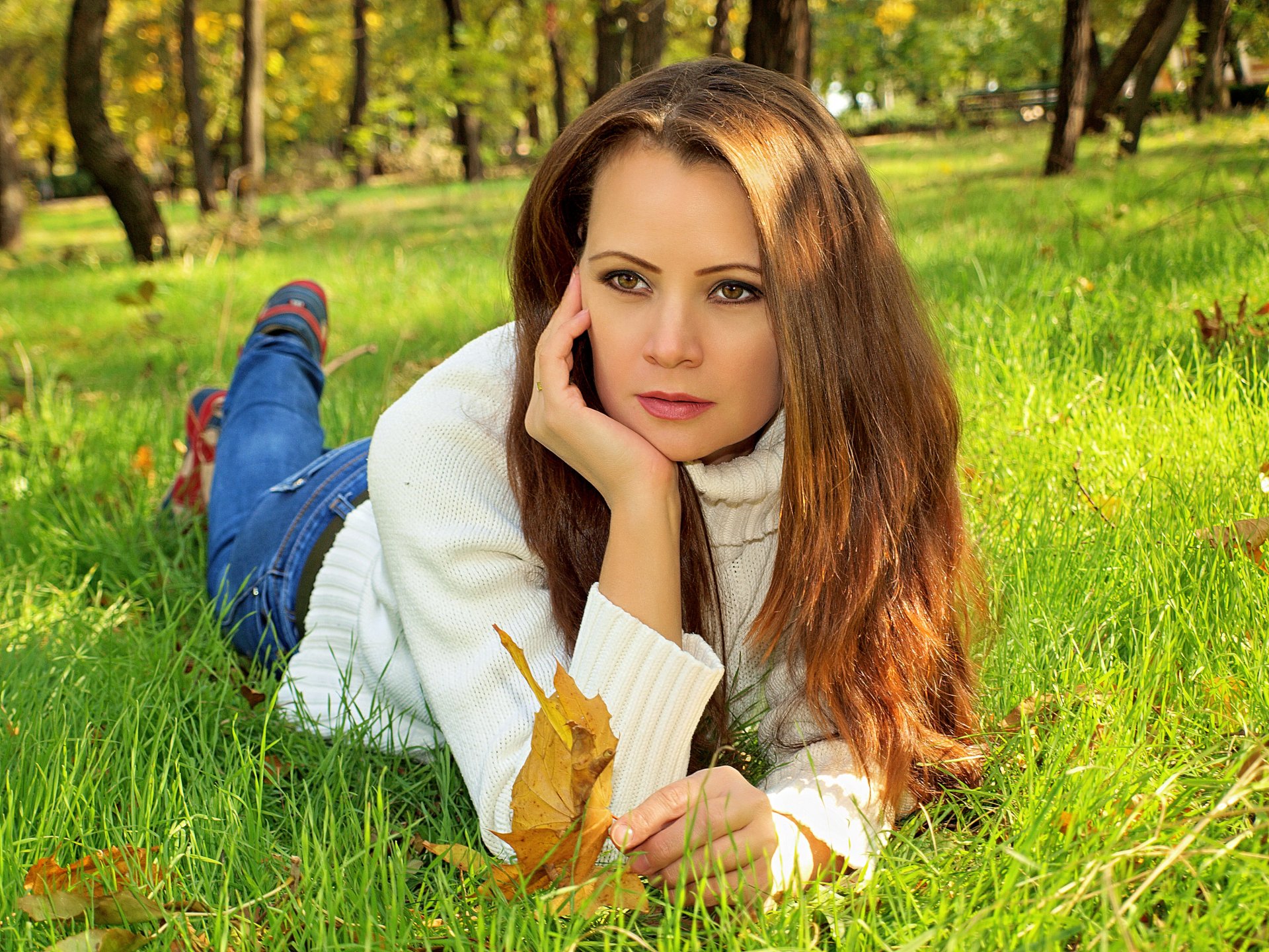 autunno parco alberi ragazza capelli castani si trova sull erba maglione jeans foglie giallo verde sfocatura