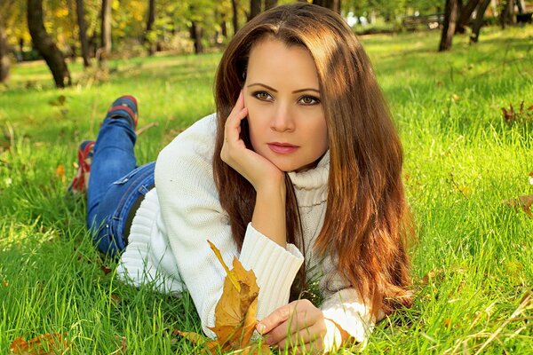 Schönes Mädchen mit langen Haaren liegt im Herbst auf dem Rasen