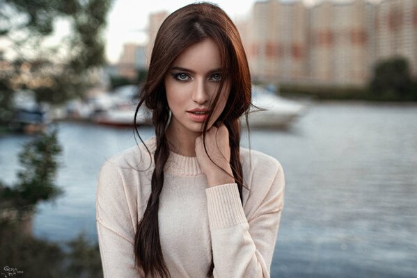 A brown-haired woman with pigtails in a white jumper, propping her chin with her hand on a blurry background