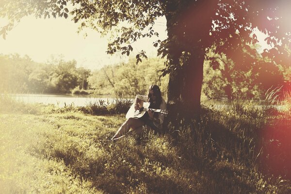 A girl on the lake shore under a tree with a guitar in her hands