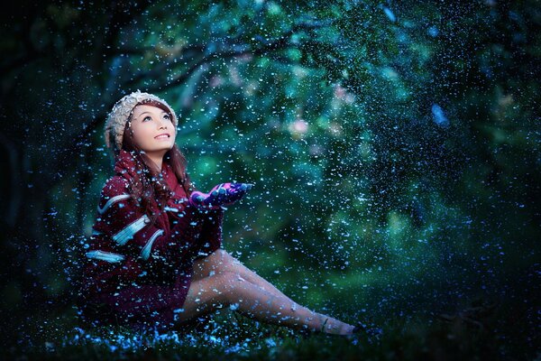 Mädchen mit asiatischer Erscheinung fängt Schneeflocken mit ihren Handflächen