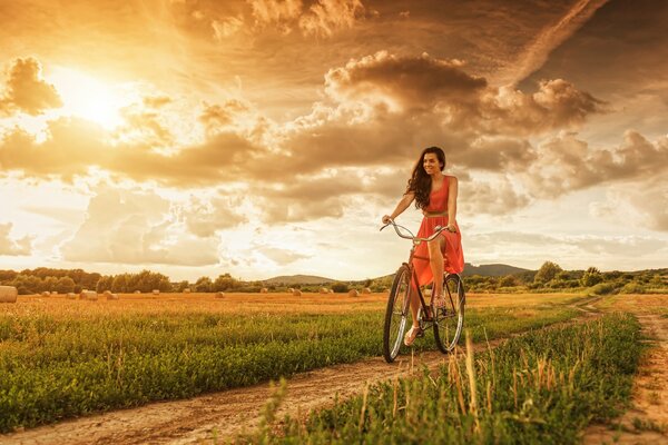 Ragazza in sella a una bicicletta sulla strada al tramonto