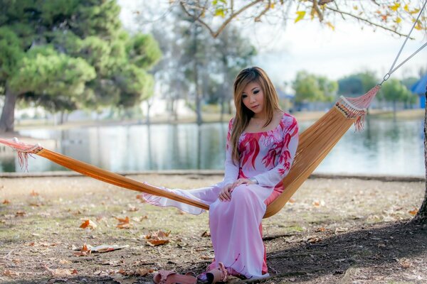 A girl is sitting in a hammock by the lake