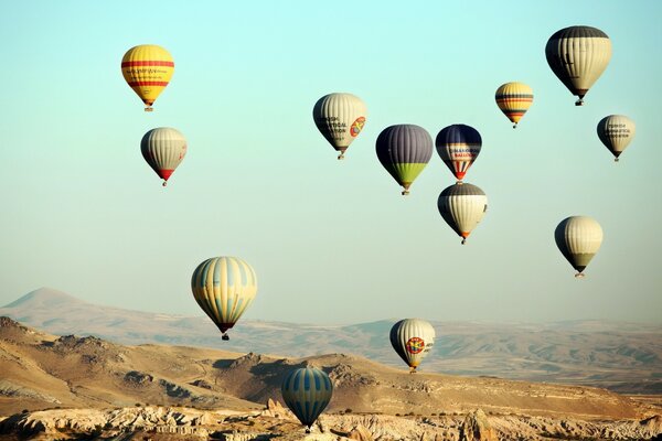 Lots of balloons flying in the sky over the hills