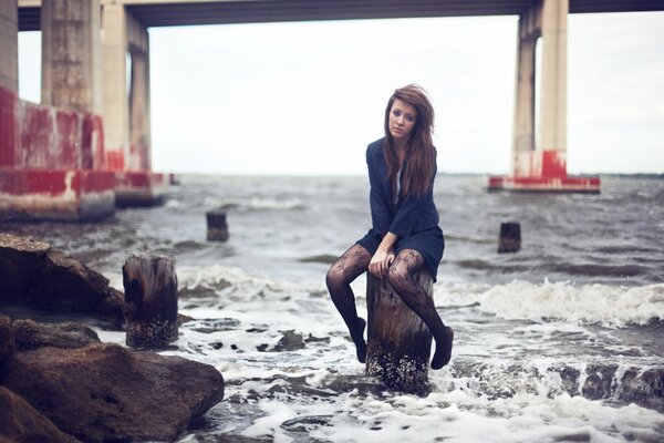 Brunette assise sur un poteau au bord de la mer