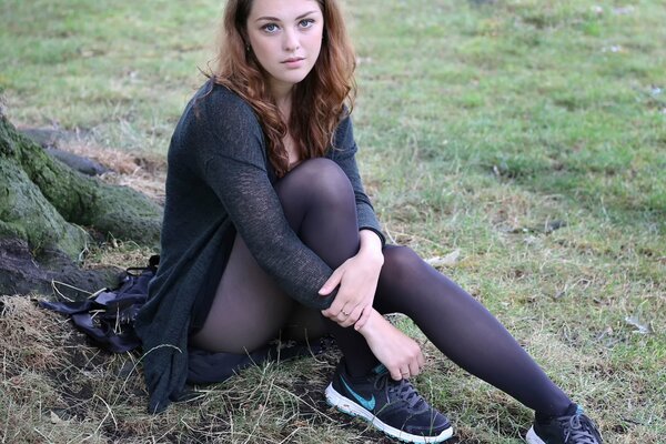 The girl is sitting on the grass in a dress and sneakers