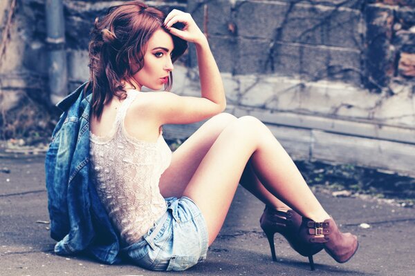 A girl in shorts is sitting on the asphalt