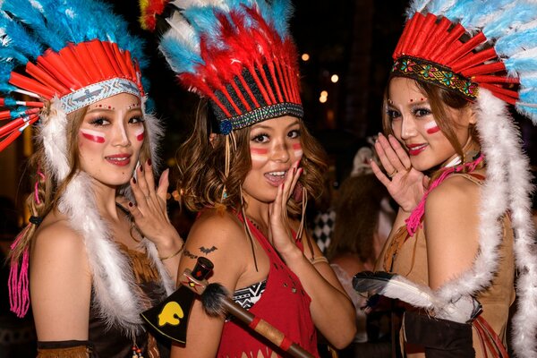 Three girls smile and pose with feathers on their heads