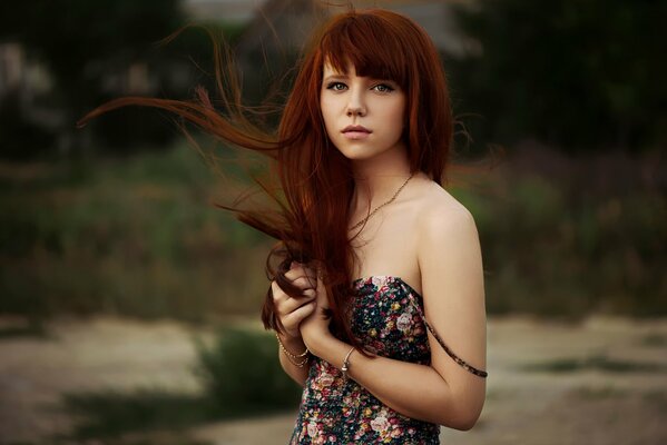 Red-haired cute girl with developing hair and a flower dress