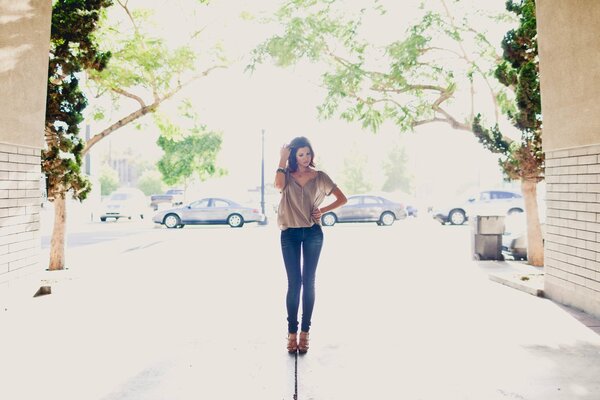 The girl is standing in the yard in a blouse and jeans