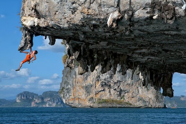 A man is hanging on a chip above the sea