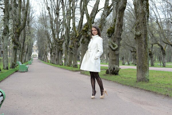 A girl in a white coat in the city garden