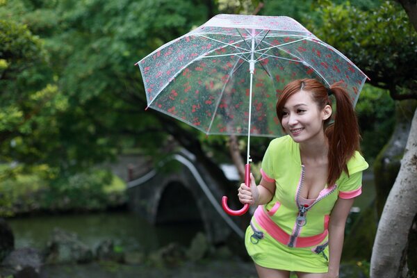 Ein asiatisches Mädchen im hellgrünen Anzug mit Dekolleté lächelt unter einem transparenten Regenschirm an der Brücke