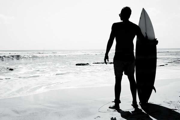 A male surfer stands by the ocean