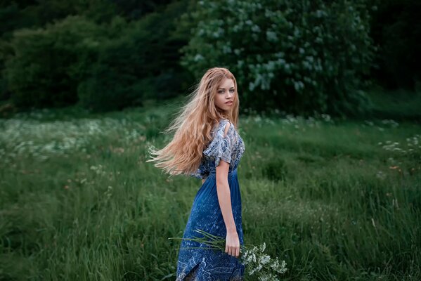 Ein entzückendes Mädchen mit einem charmanten Blick auf langes Haar in der Natur mit einem Blumenstrauß