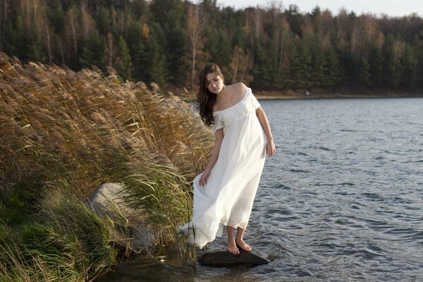 Fille en robe blanche flottant dans le vent, sur la rive de la rivière