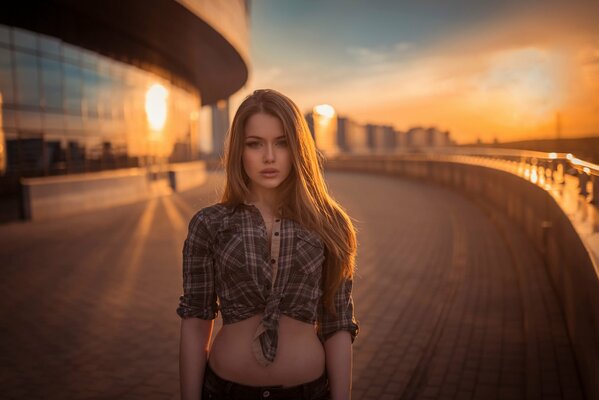 Sur fond de coucher de soleil, une jeune fille aux cheveux longs lâches dans une chemise à Carreaux nouée au-dessus de la ceinture