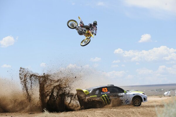 A motorcyclist soaring over a sports Subaru participating in a competition