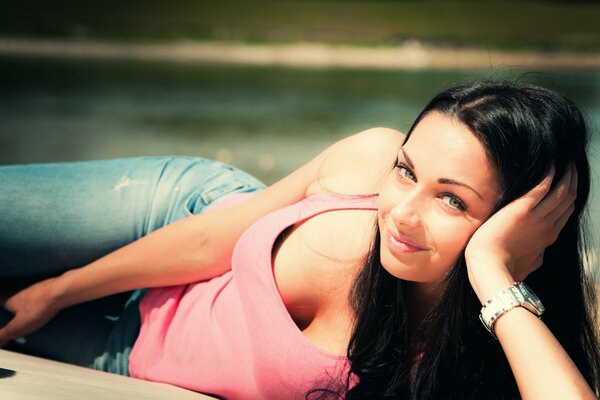 The girl is lying on her side in blue jeans and a pink T-shirt