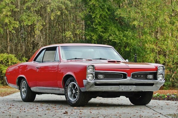 Красный hardtop pontiac classic 1967 на фоне зеленого леса