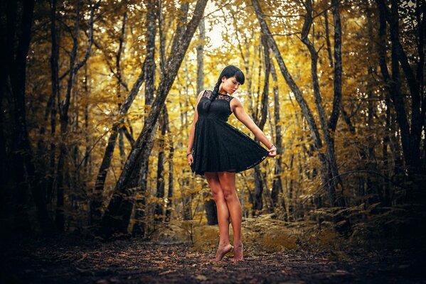 Morena en vestido negro en el bosque de otoño