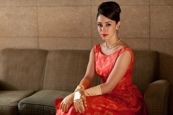 A brunette in a red dress is sitting on the couch