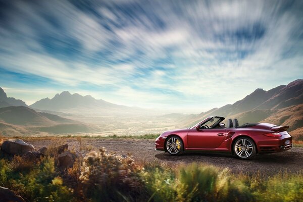 A red Porsche convertible is driving on a sandy road