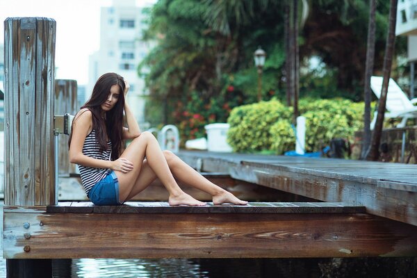 A girl in shorts is sitting by the river