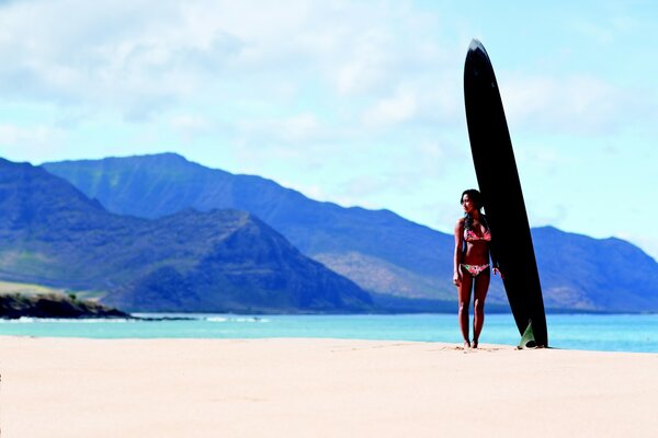 A girl with a surfboard on the background of mountains and the ocean