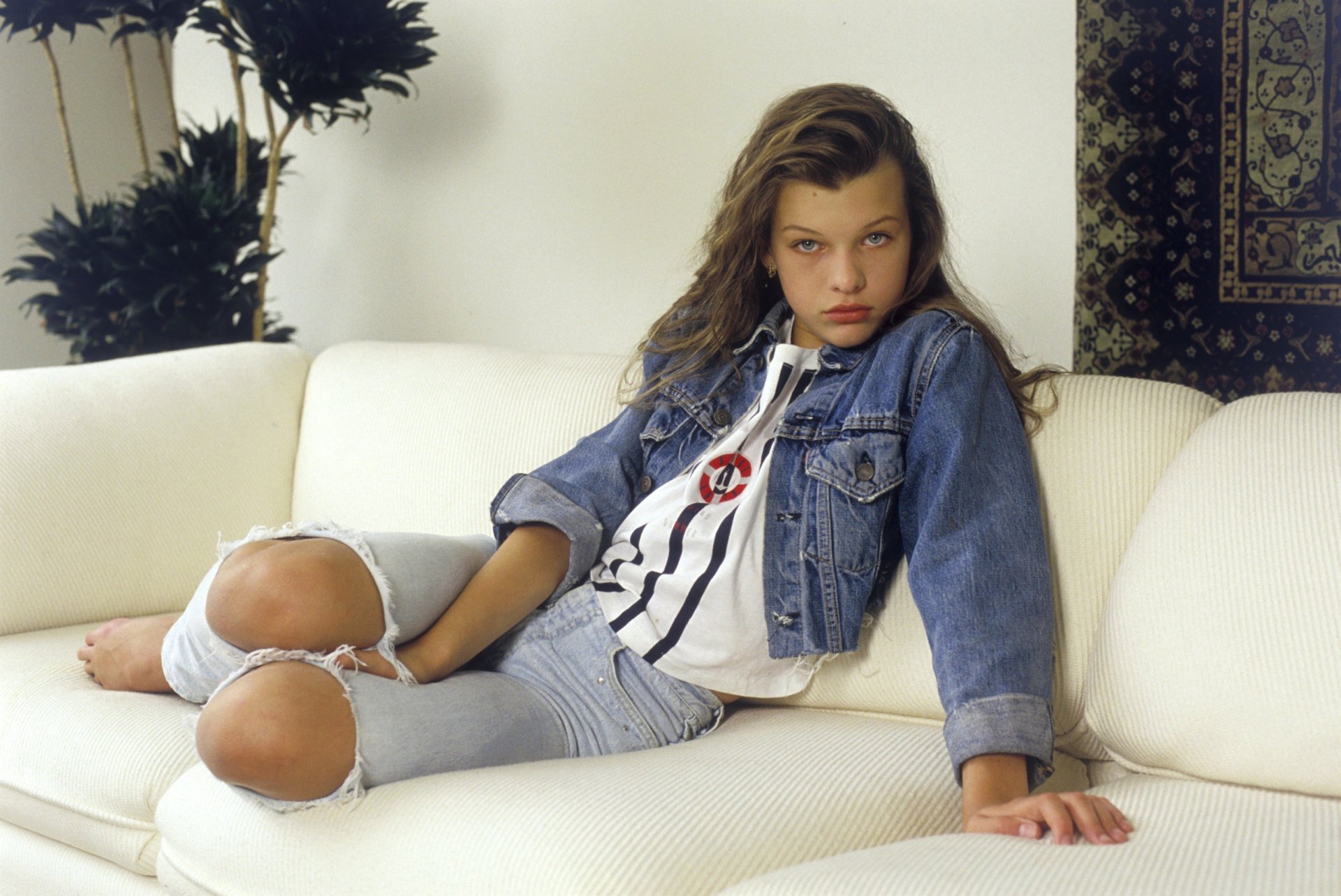 famoso attrice mila jovovich giovane ragazza mila promettente promettente mila jovovich modello jovovich sguardo atterraggio hollywood arte film film bambino bruna bellezza capelli lunghi occhi jeans gilet giacca divano posa