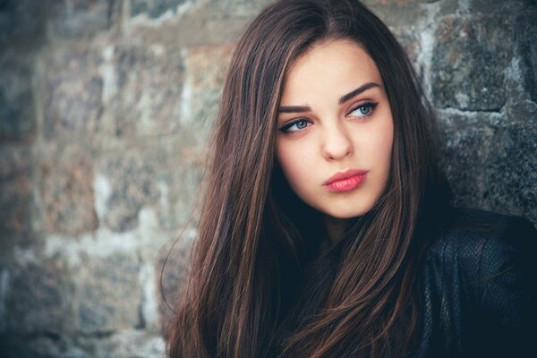 Brünette mit blauen Augen blickt vor dem Hintergrund der Wand zur Seite