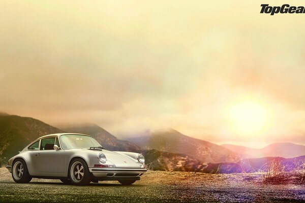 A gray Porsche stands against the sunset