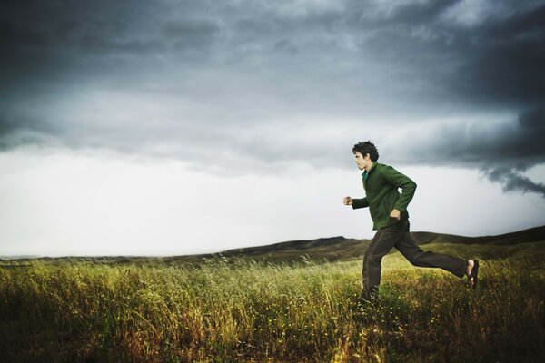 Uomo che corre attraverso il campo con tempo nuvoloso