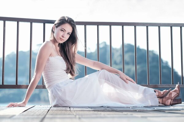 Fille en robe blanche est assis sur le plancher du balcon