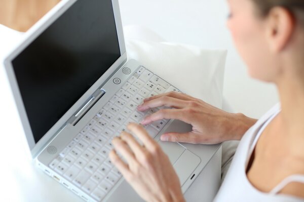 A girl with thin hands writes on a white laptop