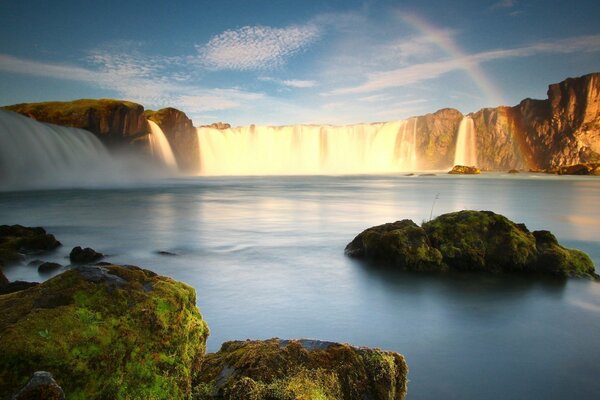 Regenbogen auf dem Hintergrund von Wasserfall und Moos